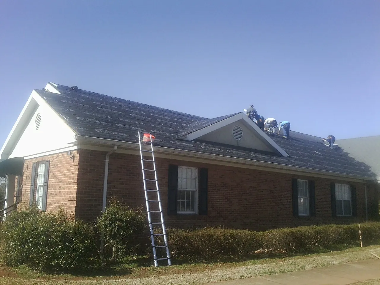 Crew tearing shingles off a brick ranch roof with a ladder set — Emergency Roof Repair work by our crew in Summer Lake