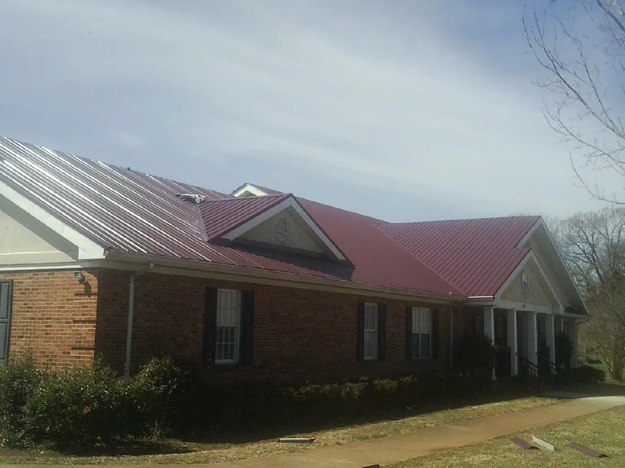 Red metal roof with gabled entries on a long brick building, from a Hail Damage Roof Repair job in Summer Lake