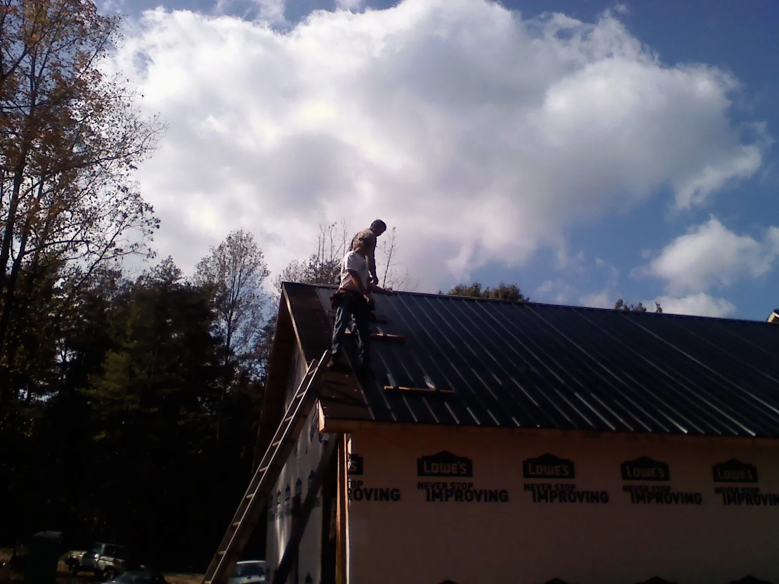 Roofer fastening dark metal panels high against a cloudy sky, from a Roof Inspection job in Summer Lake