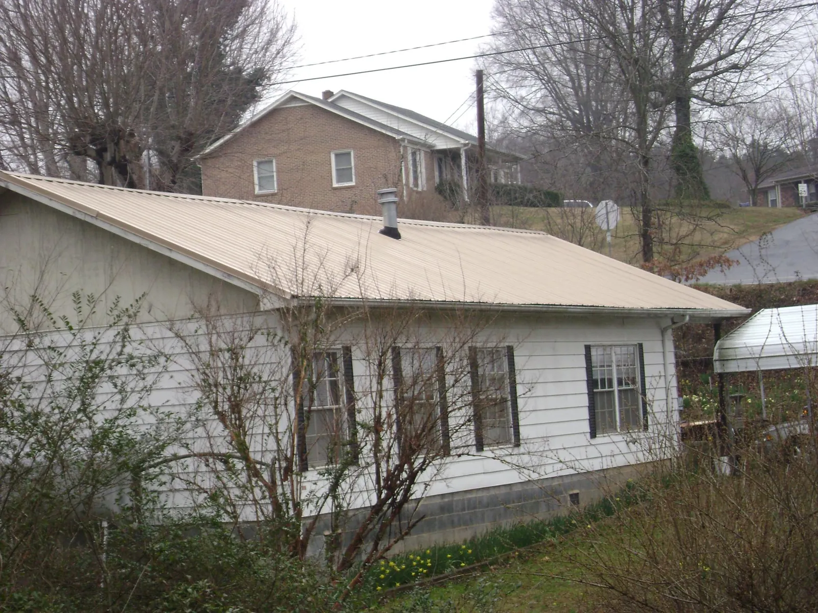 Tan metal roof on a white sided house set into a hillside — Commercial Roofing by Roofing Brothers in Summer Lake